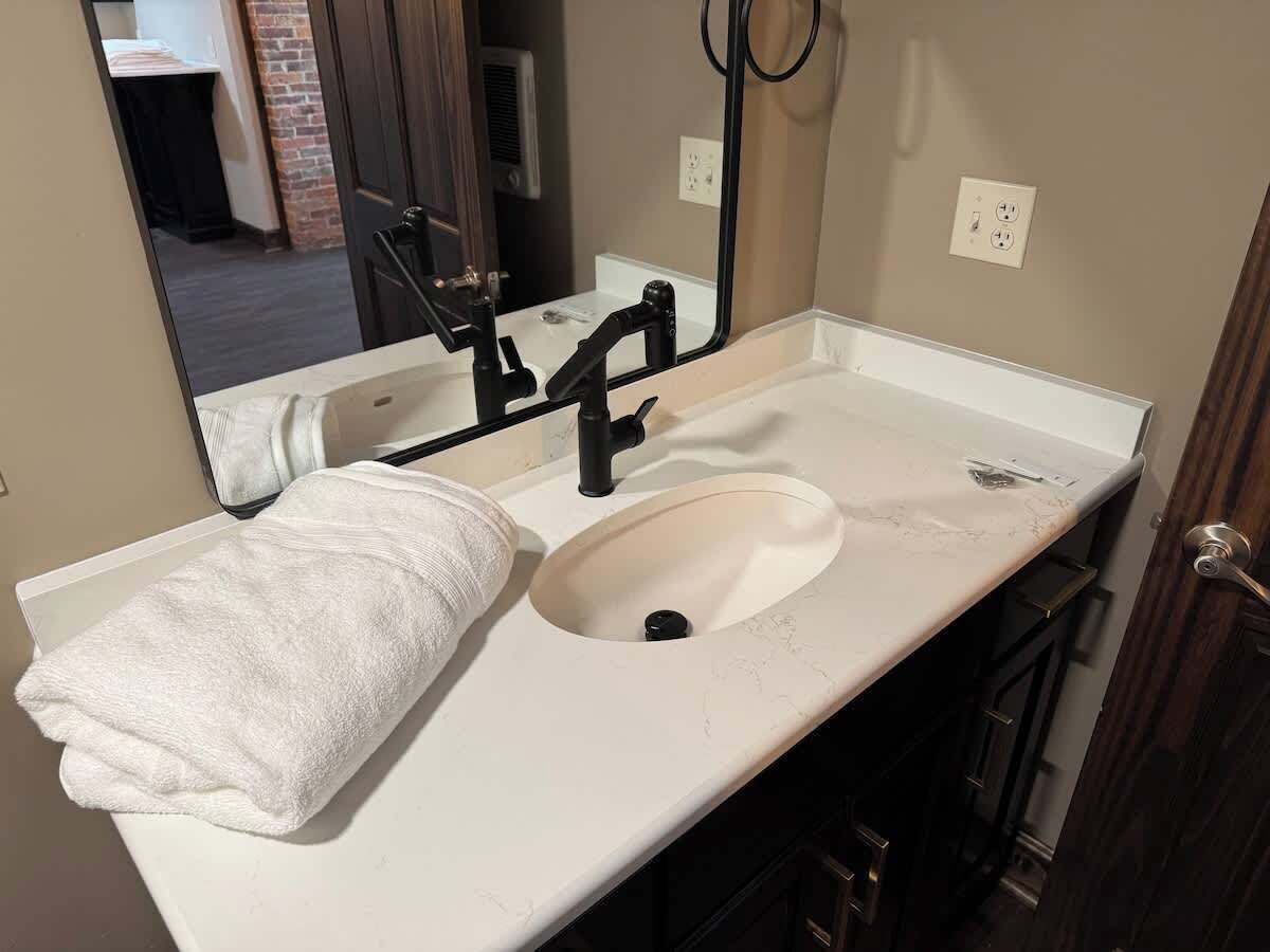 A bathroom with a white sink, a towel, a mirror, and a black faucet.