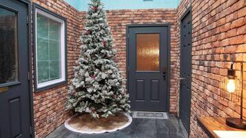 A brick-walled hallway with a frosted Christmas tree, a dark door, and a light fixture.