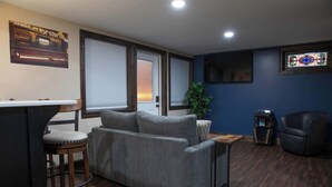 Una sala de estar con un sofá gris, una silla de madera, una mesita, una planta y un sillón de cuero oscuro.