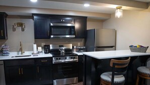 Una cocina moderna con armarios oscuros, electrodomésticos de acero inoxidable y encimera blanca.