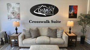 Ein gemütliches Wohnzimmer mit einer Couch und einem Hocker, einem Wandschild für die Trails to Ales Brewery und zwei Nachttischen mit Lampen.