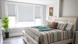 Ein Schlafzimmer mit einem Bett, einem Nachttisch, einer Topfpflanze und einem Fenster mit Jalousien.