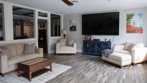 Ein Wohnzimmer mit einer Couch, einem Sessel, einem Hocker, einem Couchtisch und einem Fernseher.