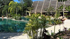 Un complex turístic amb una piscina, vegetació exuberant i un edifici gran amb nombrosos balcons.