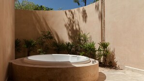 Banyera d'hidromassatge circular en un ambient exterior modern, amb una paret beix i plantes en testos.