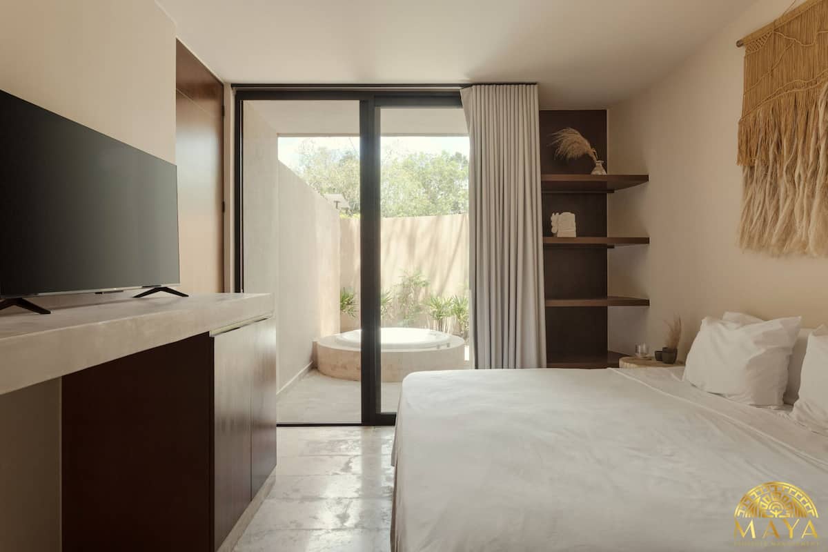 Una moderna camera d'albergo con un grande letto, una televisione a schermo piatto, un piccolo angolo salotto con un tavolino rotondo e un balcone con vista sul verde.