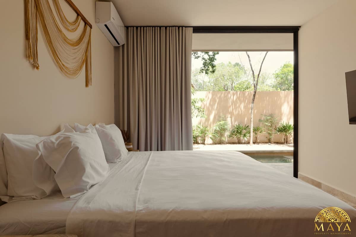 Una camera da letto con un letto, una finestra con tende e vista su uno spazio esterno con piante.