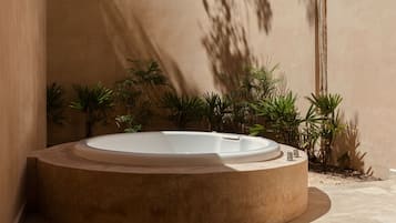 A circular hot tub in a modern outdoor setting with a beige wall and potted plants.