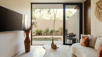 A modern living room with a sofa, a coffee table, and a large window offering a view of a pool and greenery.