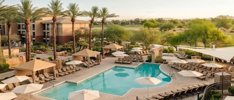 A pool area with lounge chairs and umbrellas, surrounded by palm trees and a building.