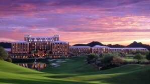 A large hotel with multiple buildings, a well-maintained golf course, and a lake in the foreground.