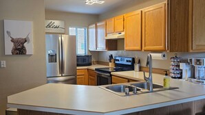 Une cuisine moderne avec des meubles en bois, un grand îlot central doté de tabourets, des appareils en acier inoxydable et un luminaire suspendu au plafond.