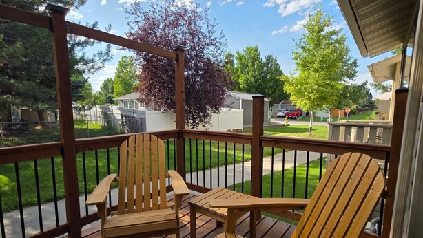 Une terrasse en bois avec deux fauteuils Adirondack et une table, donnant sur un quartier résidentiel avec des maisons et un arbre.