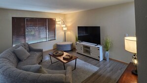 Un salon moderne avec un canapé d’angle, une table basse, un téléviseur à écran plat, une lampe et une plante.
