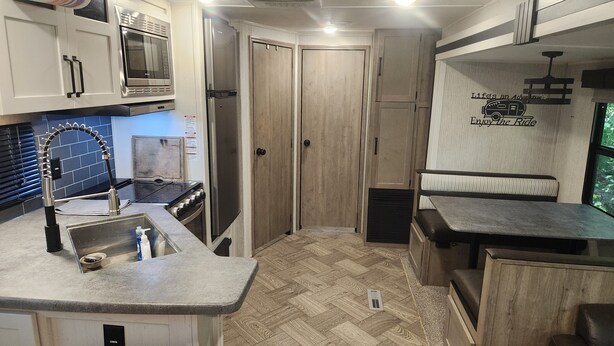 A compact kitchen with a herringbone floor pattern, a stainless steel refrigerator, a microwave, and a sink with a modern faucet. - Nature Lover's 2-Bedroom RV Escape (Hamilton)