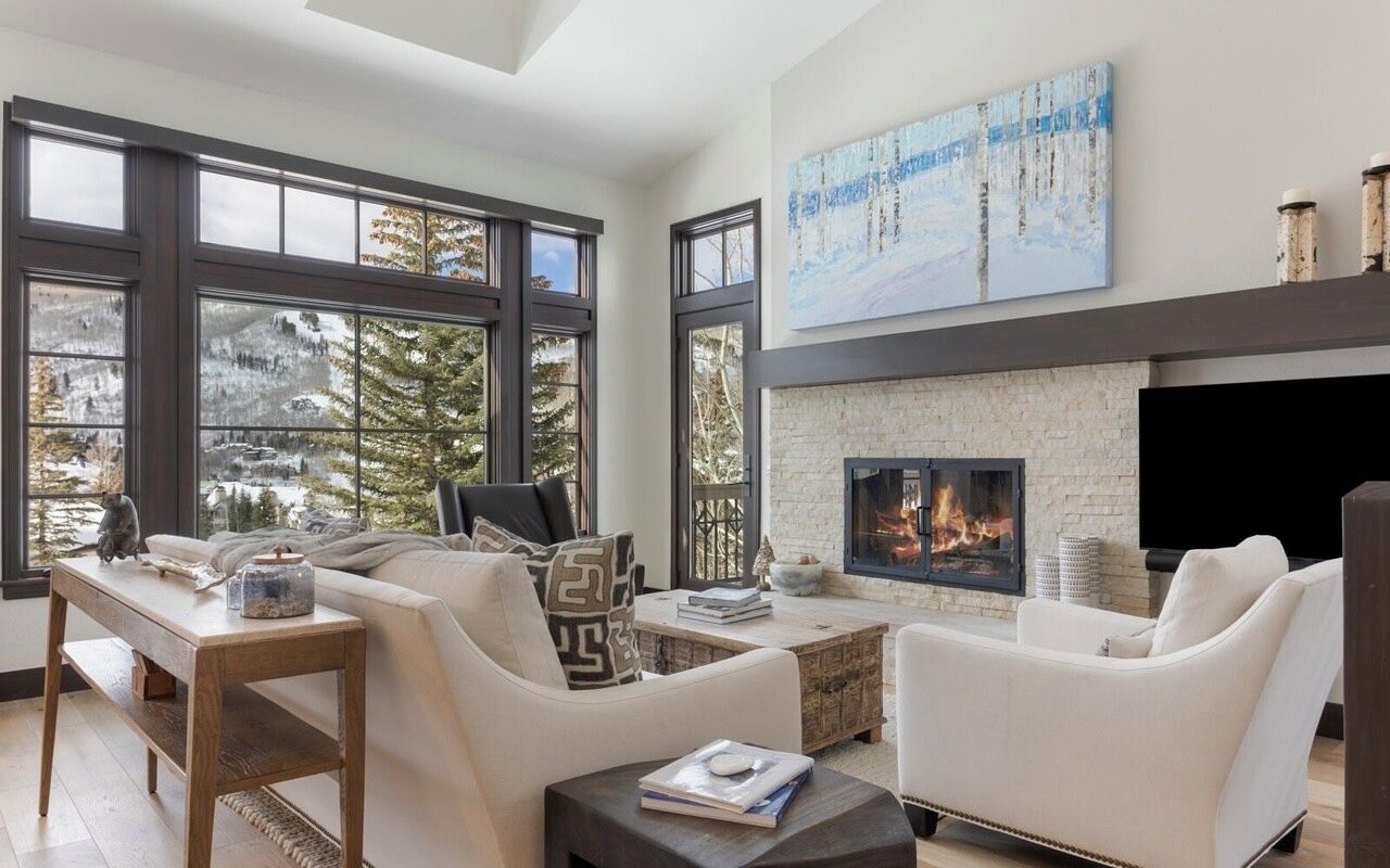 A modern living room with a fireplace, large windows, and a view of trees.