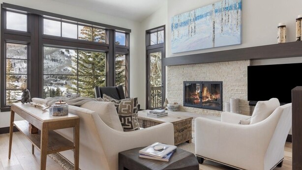Una sala de estar moderna con chimenea, ventanas amplias y vistas a árboles.