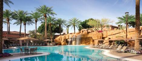 Ein Resort-Pool mit Palmen, Liegestühlen und einem Wasserfall.