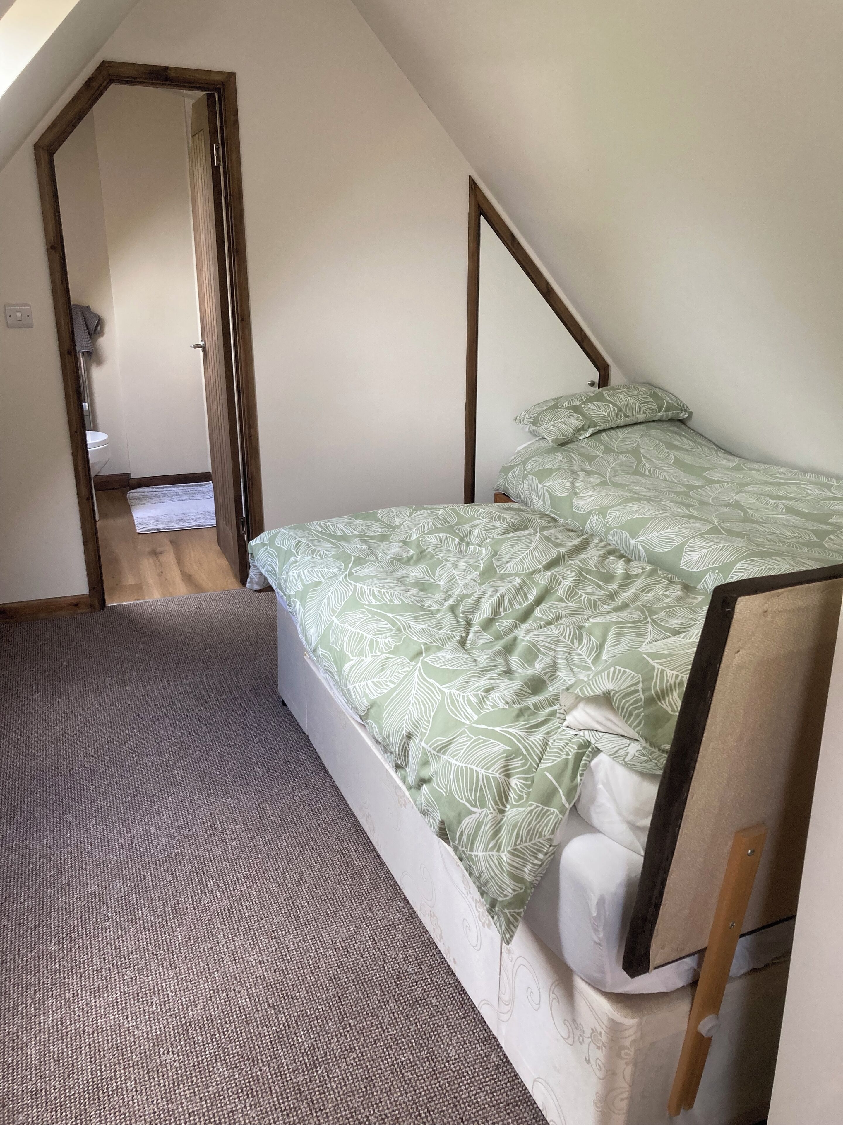Un dormitorio con cama, cabecera de madera, piso alfombrado y una puerta que da al baño.