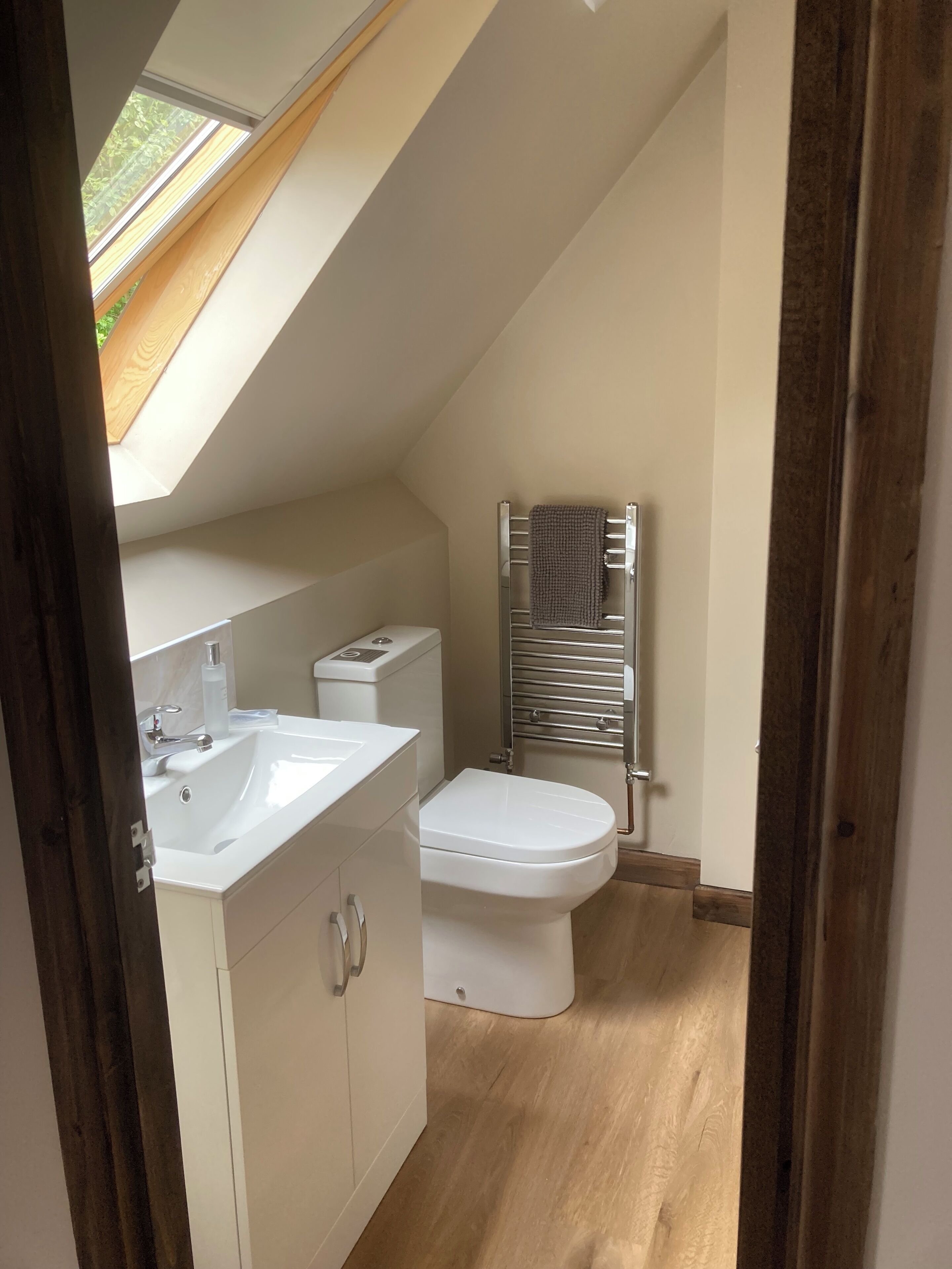 A modern bathroom with a skylight, a white sink, a toilet, and a towel rack.
