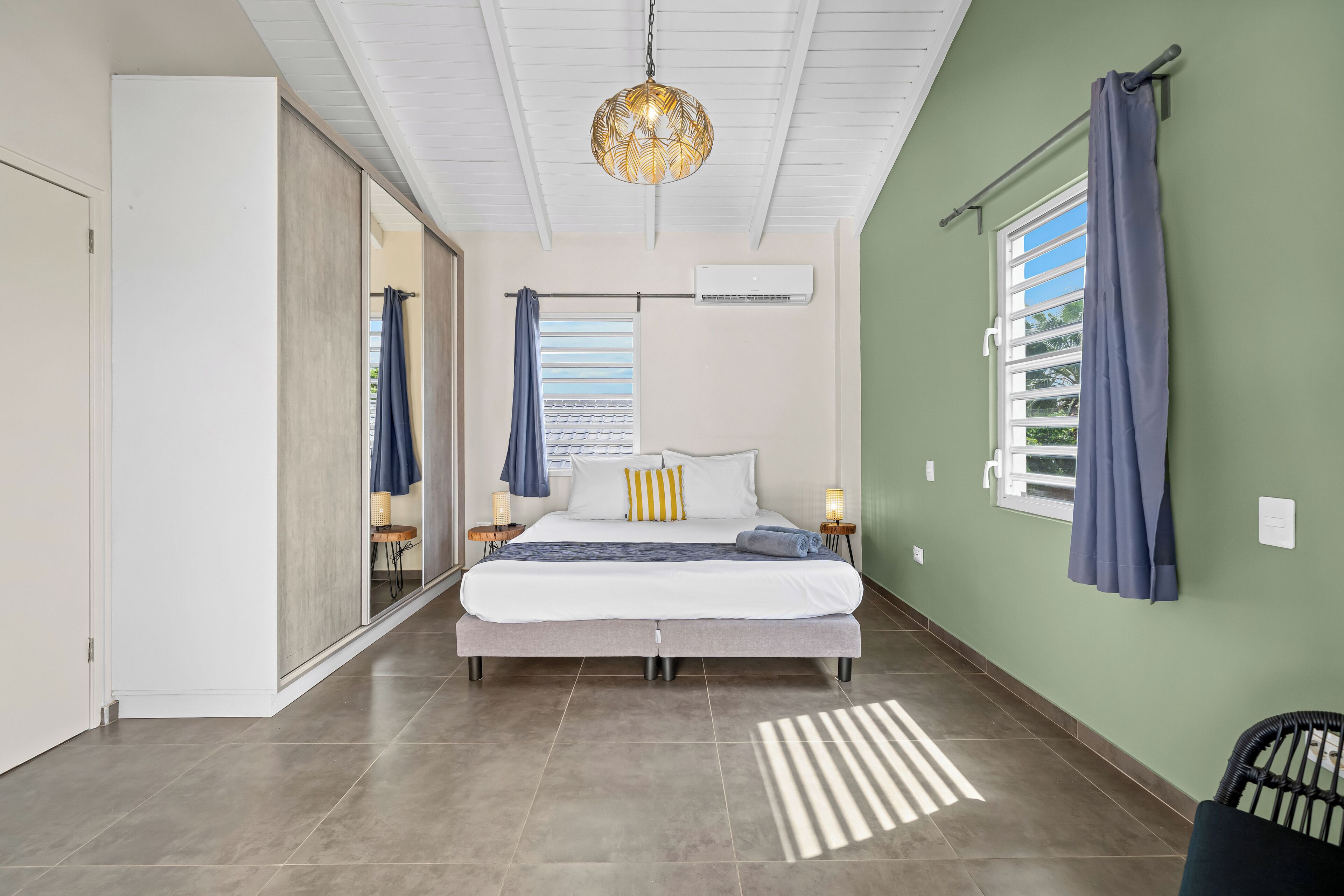 A bedroom with a bed, a ceiling fan, an air conditioning unit, and a window with curtains.