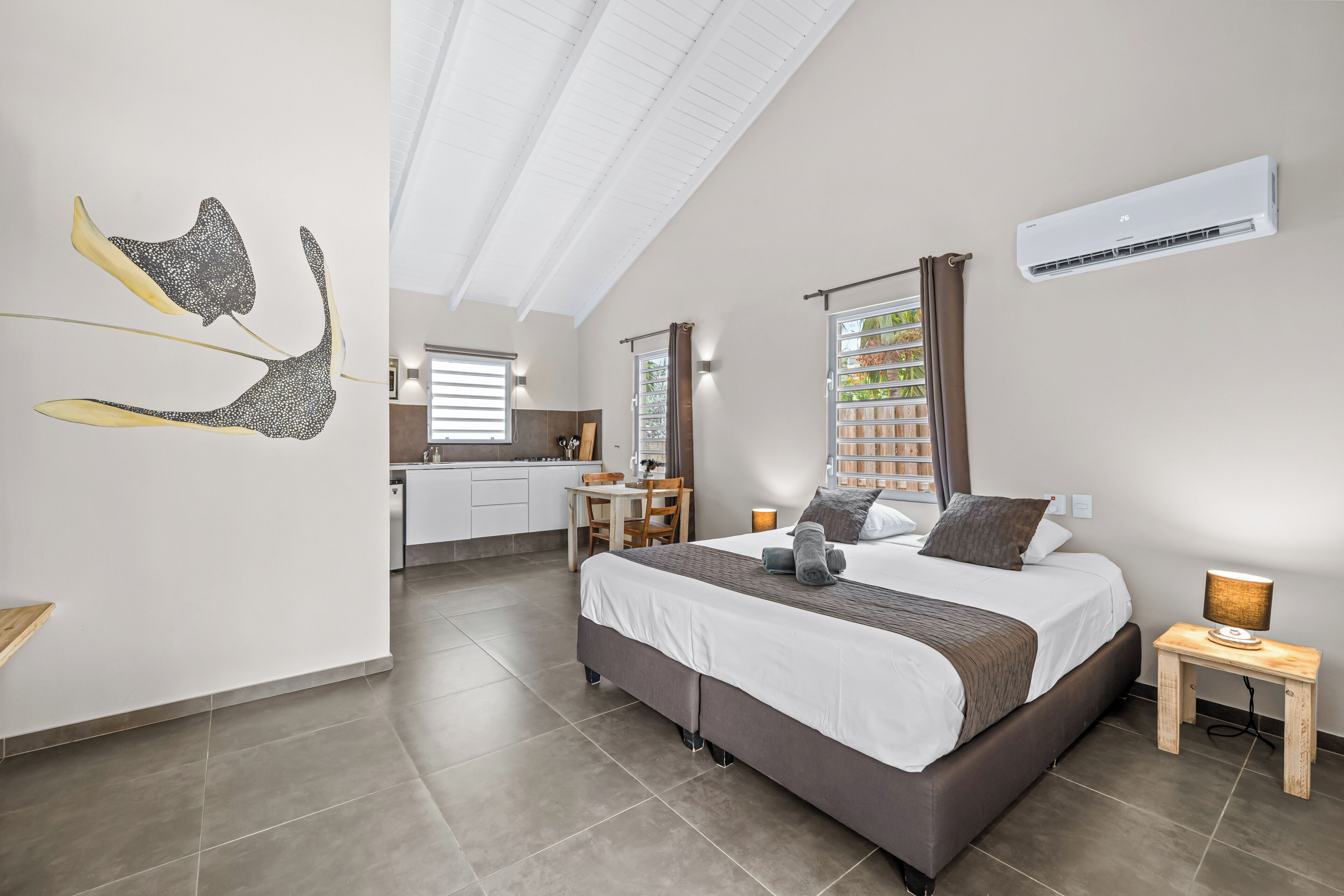 Une chambre à coucher moderne avec un grand lit, une table de chevet, une commode et une fenêtre avec des rideaux.