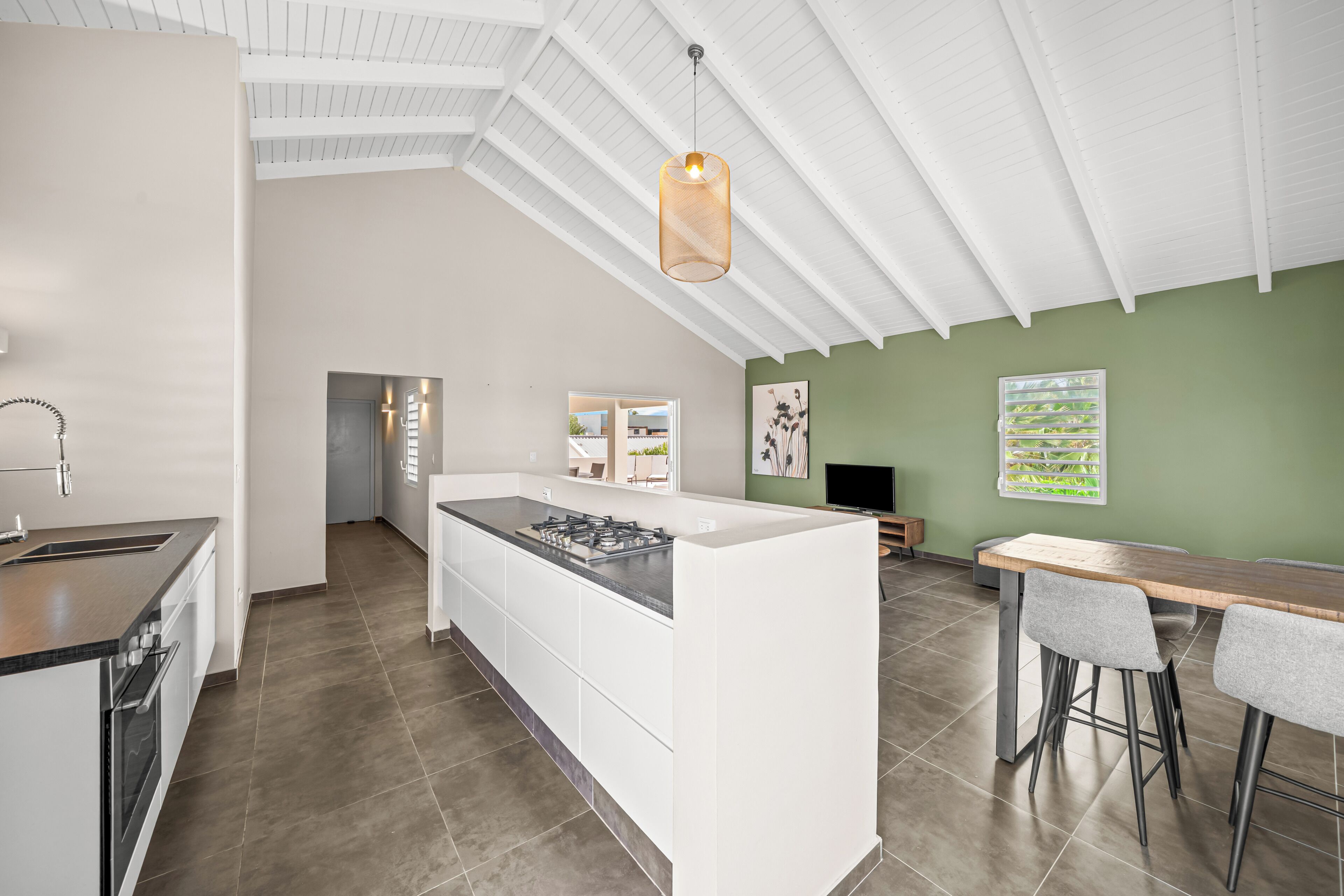 A modern kitchen with a central island, a dining area with a table and chairs, and a green accent wall.