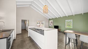 A modern kitchen with a central island, a dining area with a table and chairs, and a green accent wall.