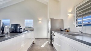 A modern kitchen with white cabinets, a stainless steel refrigerator, a built-in oven, and a large window providing natural light. - All Seasons by Boutique Bonaire Unique Resorts (Kralendijk)