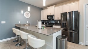 Una cocina moderna con una isla central, taburetes de bar, electrodomésticos de acero inoxidable y armarios blancos.