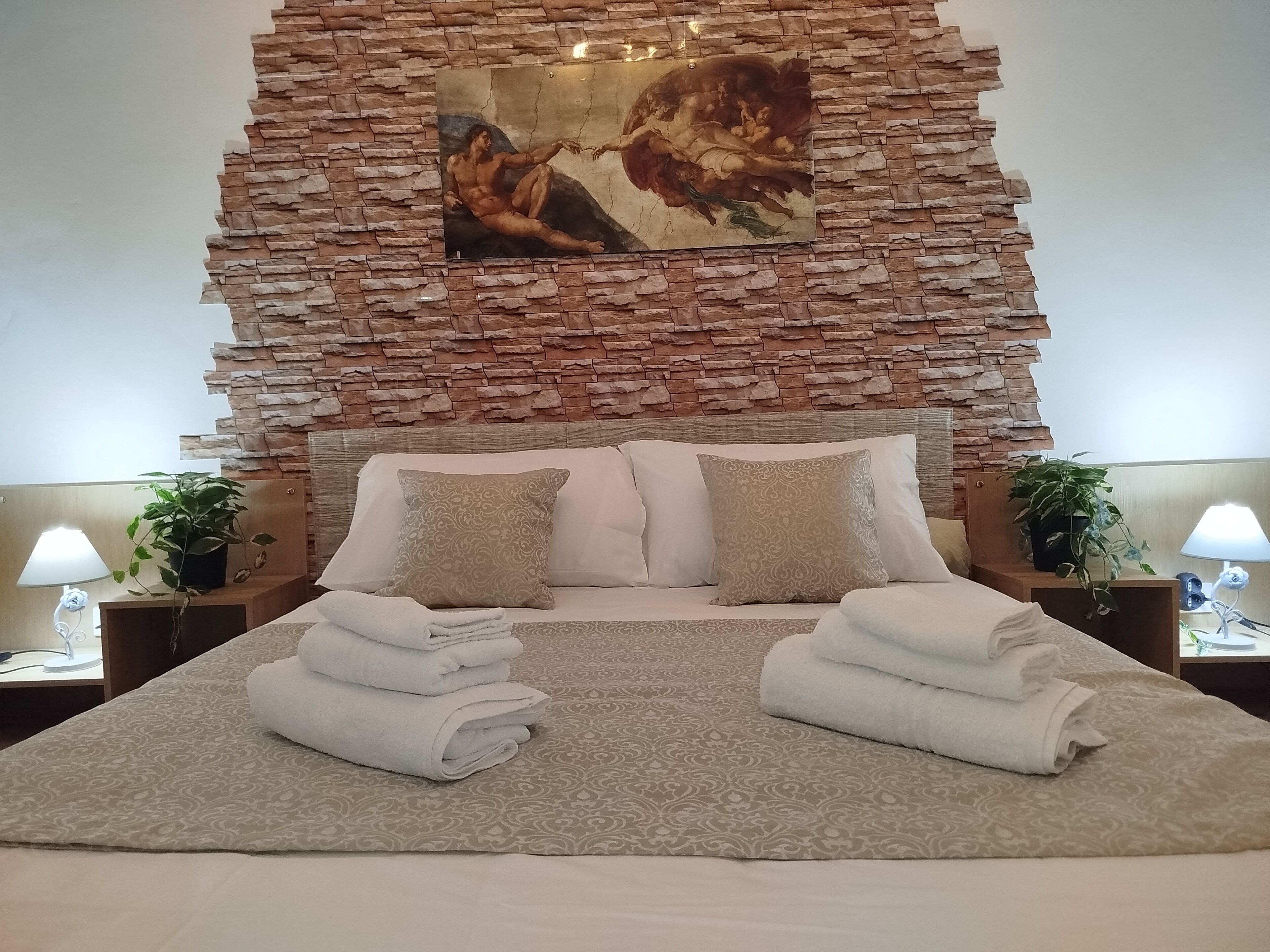 Una cama con un cabecero de pared de piedra, dos mesitas de noche con lámparas y un cuadro sobre la cama.