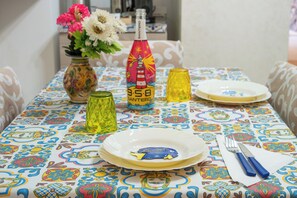 A table set with a colorful tablecloth, a vase with flowers, a bottle, and a glass.