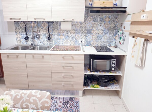 A compact kitchen with a microwave, kettle, and kettle hooks on the wall.