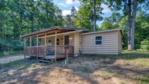 A cabin with a porch and a separate room, surrounded by trees. - Cozy Log Cabin with Dock, Kayaks, Firepit, AC, minutes to Ludington and Lake MI (Fountain)