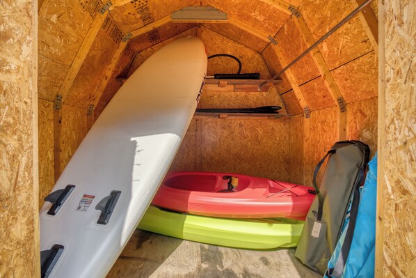 Una habitación con paredes de madera y techo inclinado, que contiene kayaks y un saco de dormir.