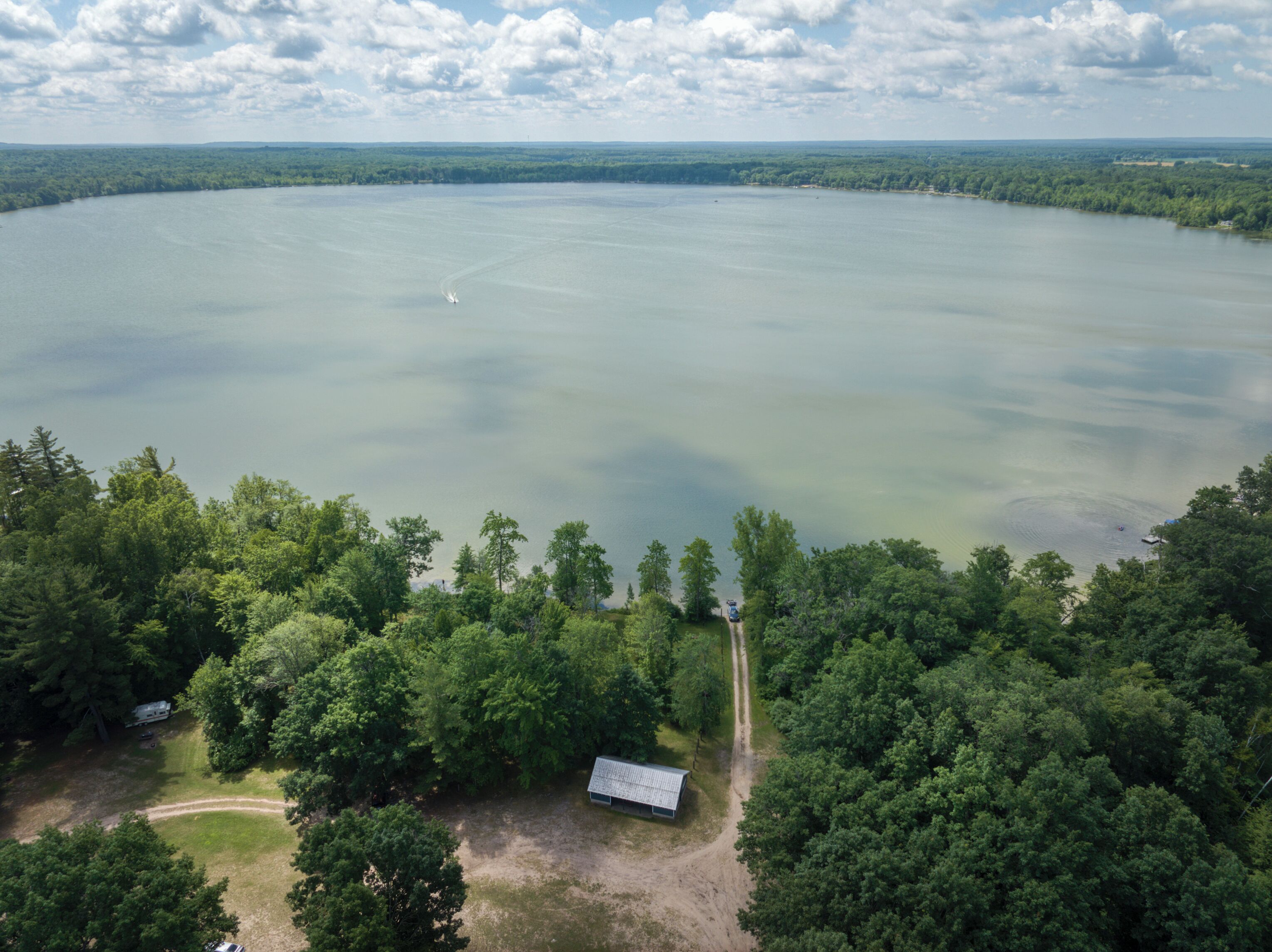An aerial view of a lake surrounded by dense forest, with a small cabin and a boat visible on the water.