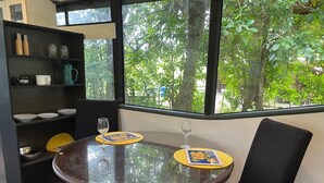 Una mesa redonda de vidrio con dos copas de vino y un mantel individual, una silla negra y una estantería con diversos objetos.
