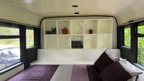 Una cama con una colcha a rayas, almohadas y un estante con libros y plantas en macetas.
