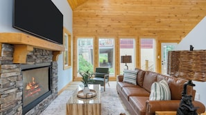 Una sala de estar acogedora con chimenea de piedra, sofá de cuero y un televisor grande.