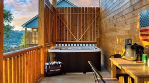 Una terraza de madera con un jacuzzi, una mesa con una mochila y una lata, y una bolsa con la etiqueta 'AVANTSTAY'.