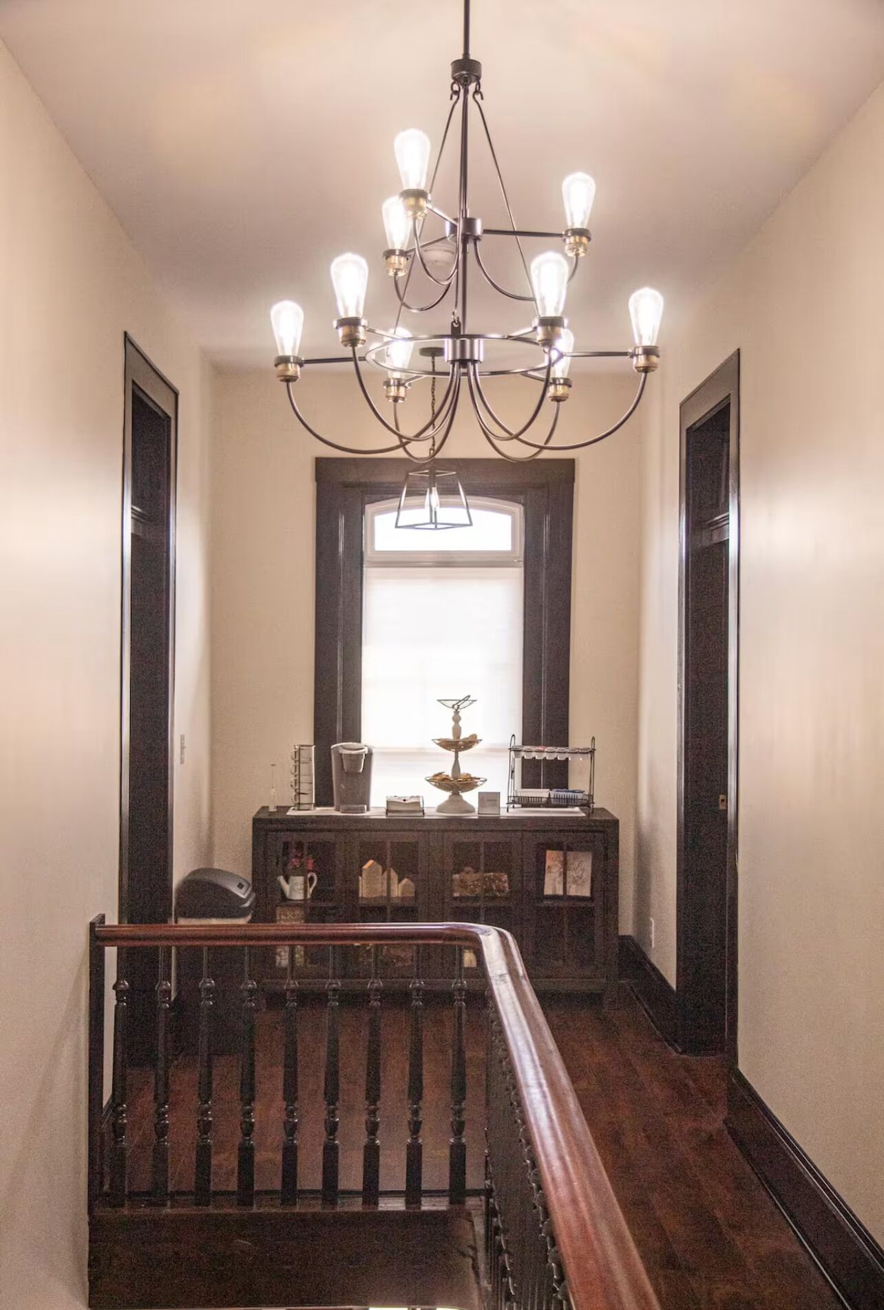 Um corredor com escada de madeira, um candelabro e uma janela com vista.