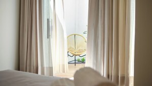 Une pièce avec des rideaux légers, un lit et, au fond, un fauteuil en osier.