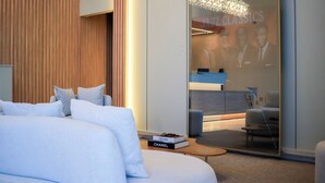 Une chambre d’hôtel moderne avec un grand lit, un petit coin salon, un mur en verre orné d’une affiche et un mur d’accent en bois.