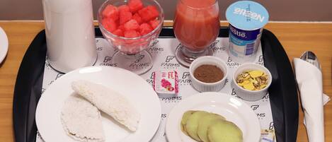 Een dienblad met eten, waaronder watermeloen, een glas sap, yoghurt en brood.