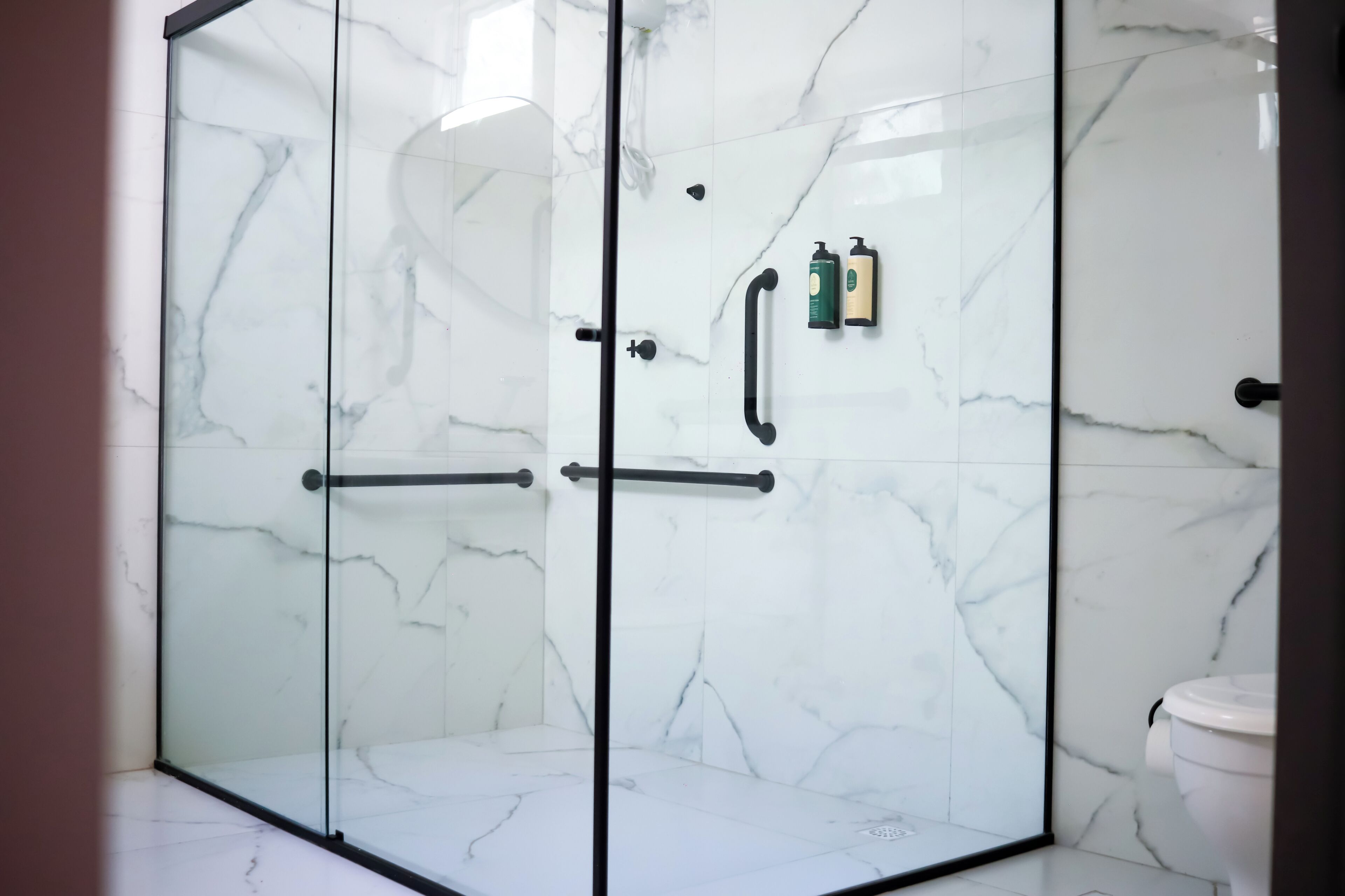 Eine gläserne Dusche mit Marmorwänden und einer rechts befindlichen Toilette.