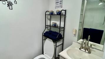 Un baño con inodoro, lavabo, espejo y repisa metálica con cuencos.
