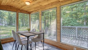 Ein Zimmer mit Holzwänden, einem Tisch und Stühlen, großen Fenstern und Blick auf ein bewaldetes Gebiet.