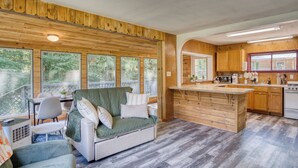 Ein gemütliches Blockhaus-Interieur mit Holzbalkendecke, einem Essbereich, einem Wohnzimmer mit Sofa und einer Küche mit Holzausstattung.