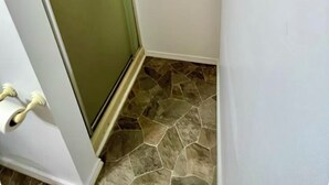 Een hoek van een kamer met een witte deur, een glazen paneel en een vloer van stenen tegels.