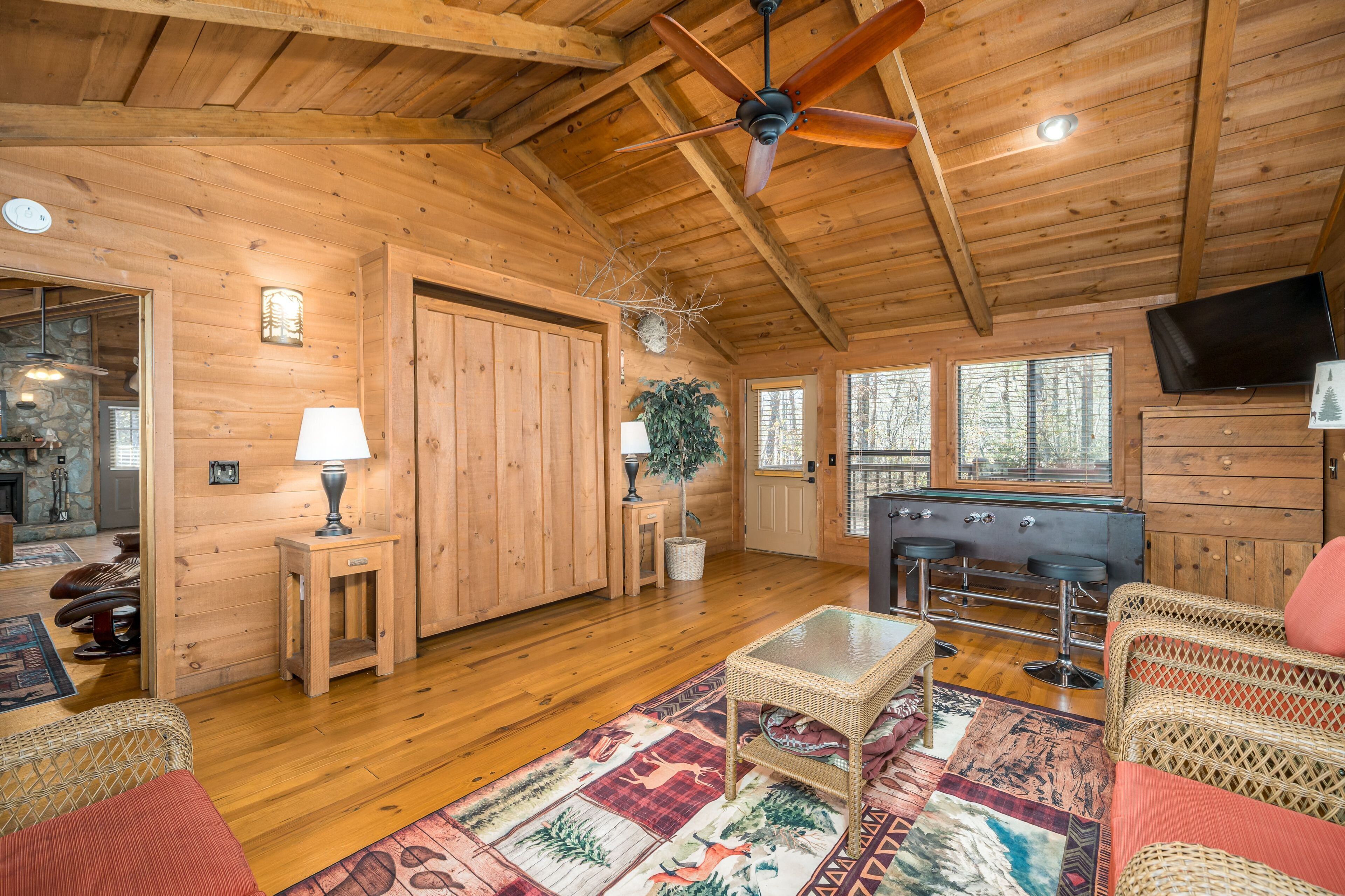 A wooden cabin interior with a ceiling fan, a fireplace, a television, and a bar area.